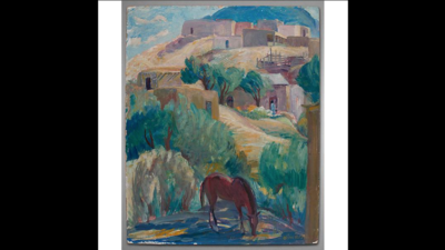 A brown horse grazes in the foreground of a hilly landscape with adobe buildings and green trees under a partly cloudy sky. [gen-ai]