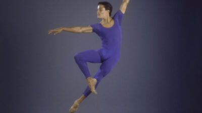 Male ballet dancer mid jump with left arm overhead and right arm extended perpendicularly