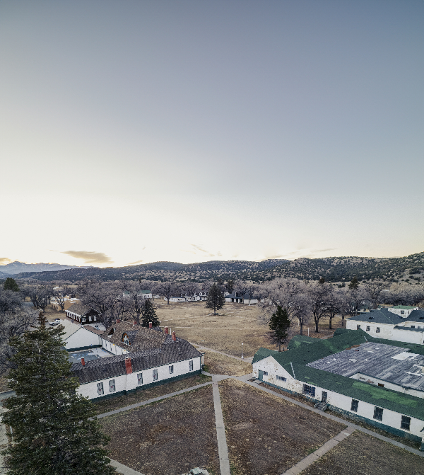 Aerial view of the Fort Stanton parade ground with the Visitor Center/ Museum on the left and the Barracks/Dining Hall on the right in the foreground. Both structures, which were originally barracks, and the parade ground date to 1855. The Sierra Blanca Mountains can be seen in the distance and are a part of the Mescalero Reservation. Photo by Tira Howard.