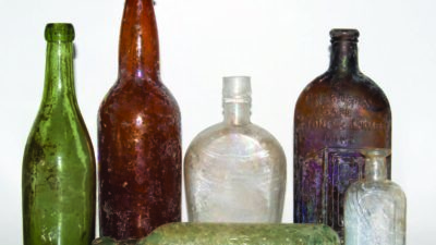 Six vintage glass bottles of various shapes, sizes, and colors are arranged against a plain white background. [gen-ai]