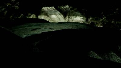 Dark, shadowy landscape with uneven terrain; faintly illuminated rocky hills or formations in the background. [gen-ai]