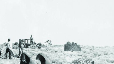 Two women in dark clothing walk through a scrubby landscape while men, horses, and a horse-drawn coach are visible in the background. [gen-ai]