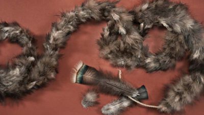 A feathered dance stick, a length of rope, and several coils of grey-brown feathered garland are arranged on a brown surface. [gen-ai]