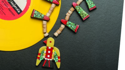 A colorful beaded necklace with a bird-shaped pendant lies on a black surface next to a yellow vinyl record. [gen-ai]