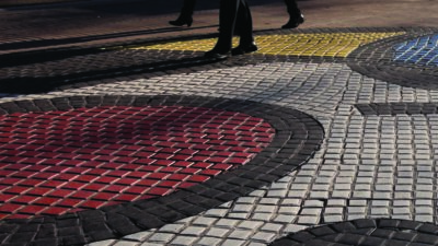 People walking on a street with a patterned sidewalk featuring circular designs in red, yellow, blue, white, and black tiles. [gen-ai]
