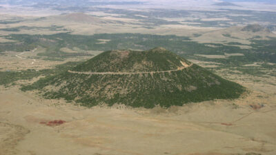 Aerial view of an isolated, cone-shaped volcanic hill with a winding road circling its slope, surrounded by flat, sparsely vegetated land. [gen-ai]