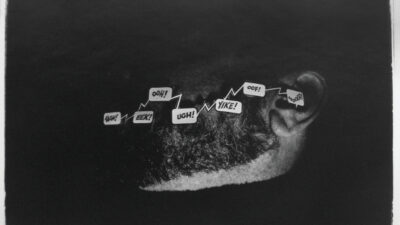 A grayscale image of a persons ear and part of their head, with comic-style speech bubbles above the ear displaying words like AAH!, EEK!, UGH!, YIKE!, and OOF!. [gen-ai]