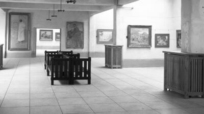 Black and white photo of an art gallery with framed paintings on the walls, wooden benches, and tiled floors. No people are present. [gen-ai]