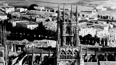 A black-and-white aerial view of a Gothic cathedral with pointed spires, surrounded by historic buildings and countryside in the background. [gen-ai]