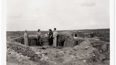 Four people stand among ancient stone ruins at an archaeological excavation site, with open landscape visible in the background. [gen-ai]