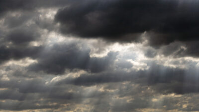 Dark clouds cover the sky as rays of sunlight break through, creating shafts of light and shadow across the cloudscape. [gen-ai]