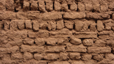 Close-up view of an uneven mud brick wall with rough texture and visible gaps between the bricks. [gen-ai]