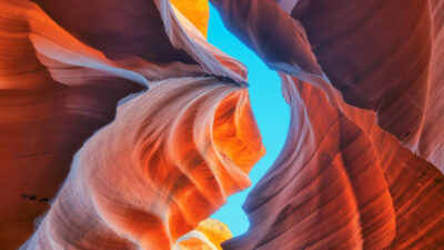 View looking up through the winding, orange and red sandstone walls of Antelope Canyon with a strip of bright blue sky above. [gen-ai]