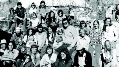 A large group of people, adults and children, posing outdoors on rocks and grass, with a dog sitting on the right side of the image. [gen-ai]