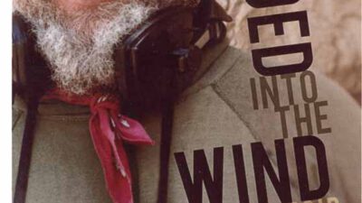 A bearded man smiling, wearing a bandana and binoculars around his neck; text reads Headed into the Wind: A Memoir by Jack Loeffler. [gen-ai]