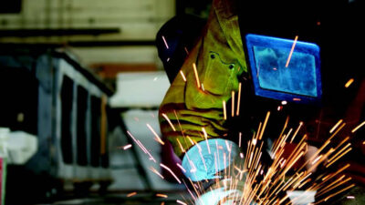 A person wearing protective welding gear uses a tool to grind metal, creating bright sparks in an industrial workshop setting. [gen-ai]