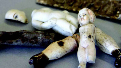 Several broken porcelain doll parts, including limbs, a torso, a head, and a fragment of an arm, are scattered on a flat surface. [gen-ai]