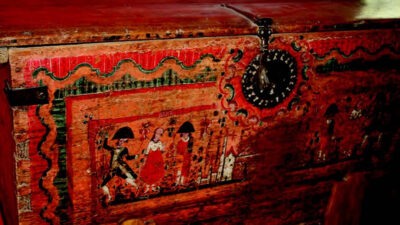 A weathered, ornately painted wooden chest with a large black metal lock and decorative patterns, featuring figures and buildings. [gen-ai]