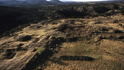 Aerial view of an archaeological site on a hillside with excavated areas and surrounding desert landscape, mountains in the background. [gen-ai]