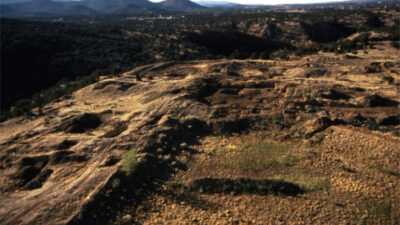 Aerial view of an ancient archaeological site on a rocky, sunlit plateau with excavation areas and mountains in the background. [gen-ai]