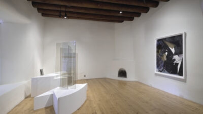 Contemporary art gallery with wooden floors, sculptural glass pieces on white plinths, a large abstract painting on the wall, and exposed wooden ceiling beams.
