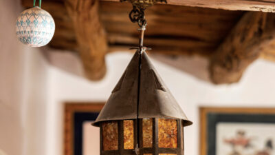 A rustic lantern with amber panels hangs from a wooden beam beside a blue-and-white ornament; framed artwork is visible in the background.
