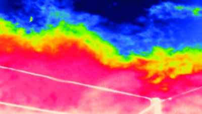 Thermal image of the sky showing temperature variations with cooler blue and warmer red areas; power lines are visible in the foreground.