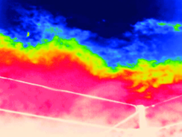 Thermal image of the sky showing temperature variations with cooler blue and warmer red areas; power lines are visible in the foreground.