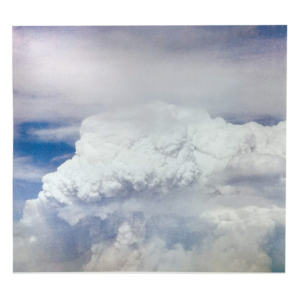 A photograph of a large, fluffy white cloud against a blue sky with subtle hints of sunlight illuminating the clouds edges.