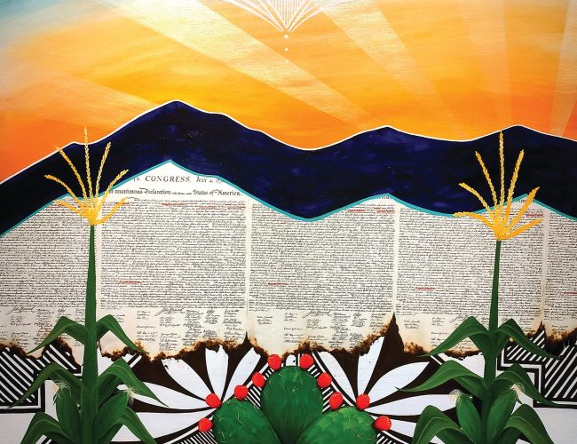 A vibrant painting shows two corn stalks and a cactus with red fruit in the foreground, a mountain range in the middle, and the U.S. Declaration of Independence text and a radiant sunrise in the background.