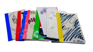 A stack of handmade, colorful booklets with illustrated and decorated covers, featuring drawings, text, and various colors of tape binding the spines, arranged on a white background.
