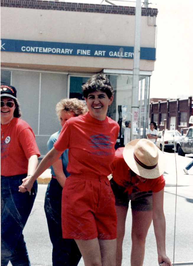 Four people wearing red shirts stand and interact on a sidewalk in front of a building labeled Contemporary Fine Art Gallery on a sunny day.